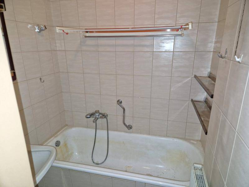 Badezimmer mit Badewanne, hellen Fliesen und einem kleinen Waschbecken, ausgestattet mit Haltegriffen.