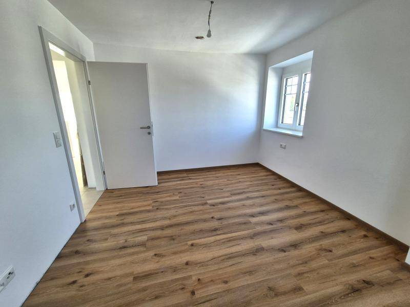 Leeres Schlafzimmer mit Laminatboden, weißen Wänden und einem Fenster, bereit zur Einrichtung.