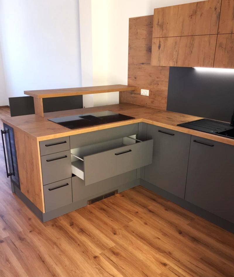 Moderne Küche mit geöffneter Schublade, grauen Unterschränken und Arbeitsplatten in Holzoptik.