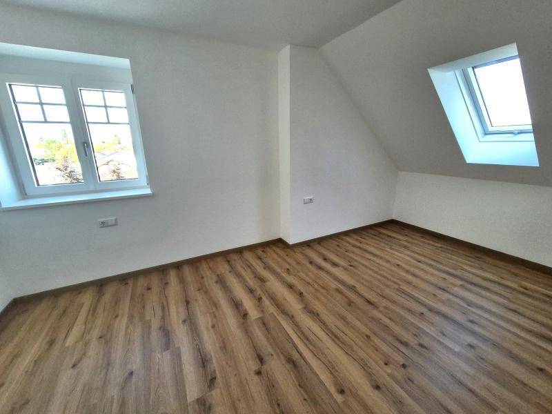 Helles Schlafzimmer mit Laminatboden, weißen Wänden, einem Fenster und einem Dachfenster.