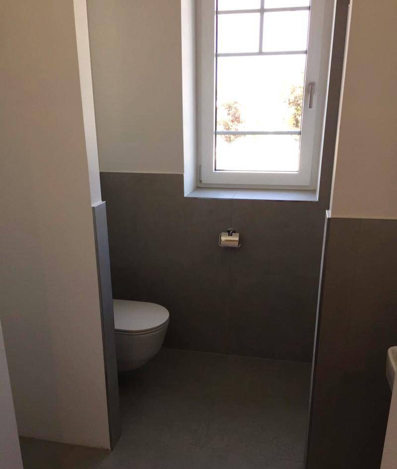 Modernes Gäste-WC mit Fenster, grauen Fliesen und einer wandhängenden Toilette.