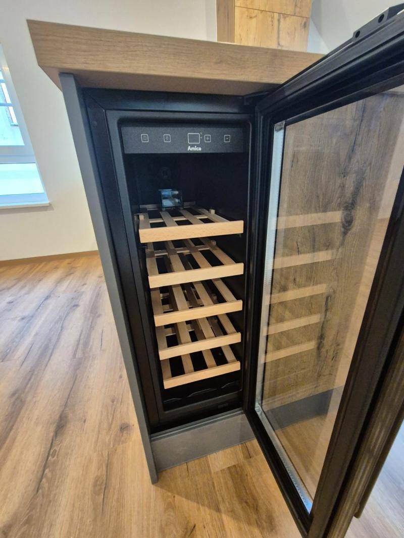 Detailansicht des integrierten Weinkühlers in der Kücheninsel, mit geöffneter Glastür und Holzregalen.
