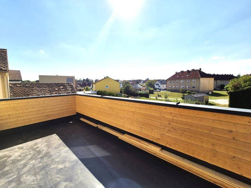 Geräumige Dachterrasse mit Holzverkleidung und weitem Blick über die umliegende Wohngegend an einem sonnigen Tag.