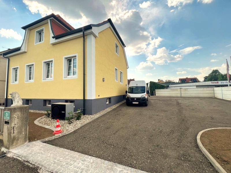 Gelbes Gebäude mit neu angelegtem Kiesparkplatz und moderner Wärmepumpe im Außenbereich.