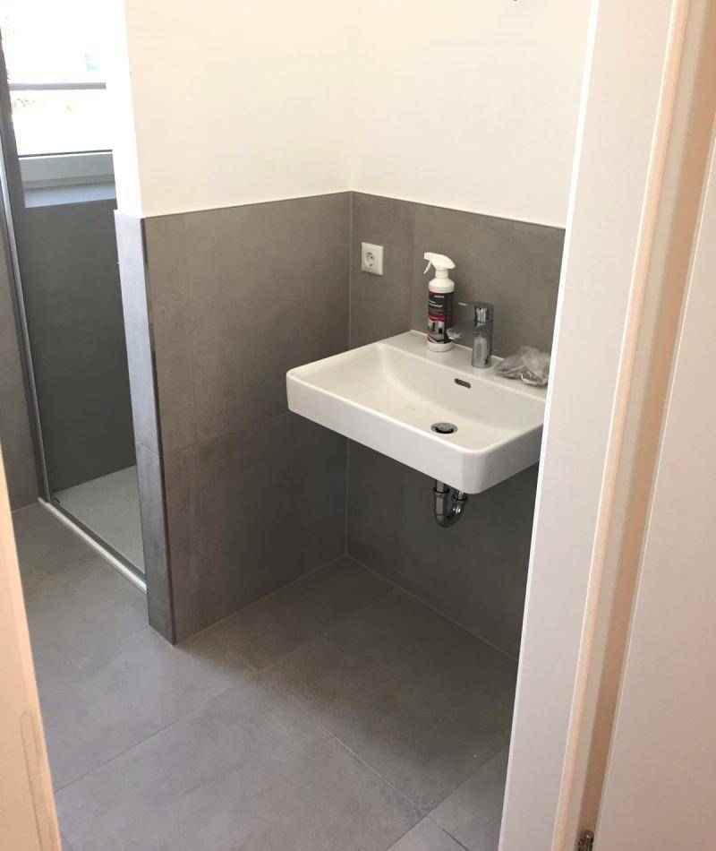 Schwebendes Waschbecken und Teil der ebenerdigen Dusche, mit modernen Fliesen an den Wänden.