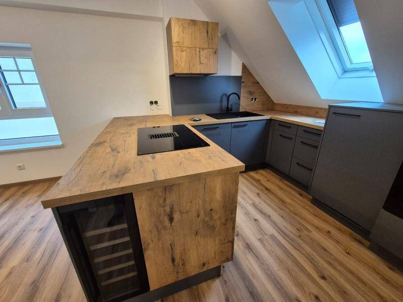 Gesamtaufnahme der modernen Küche mit Kochinsel, grauen Schränken, Holzdetails und Dachfenster.