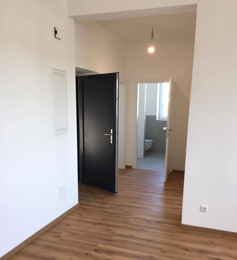 Eingangsbereich mit Laminatboden, einer schwarzen Eingangstür und Blick in ein angrenzendes Badezimmer.