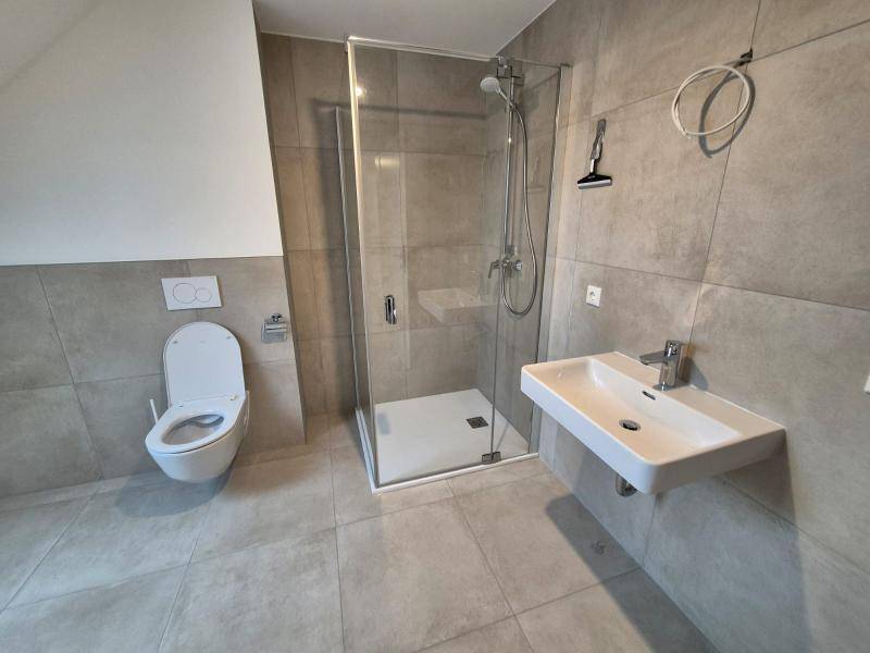 Helles Badezimmer mit Duschkabine, Waschbecken und Wand-WC, modern gefliest in Grau.