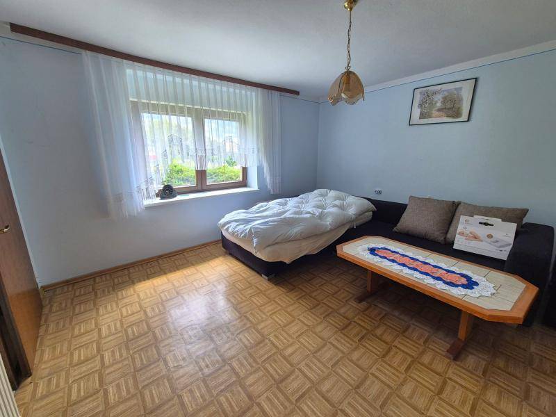 Schlafzimmer mit Parkettboden, einem Bett und einem Sofa, hell durch ein großes Fenster.