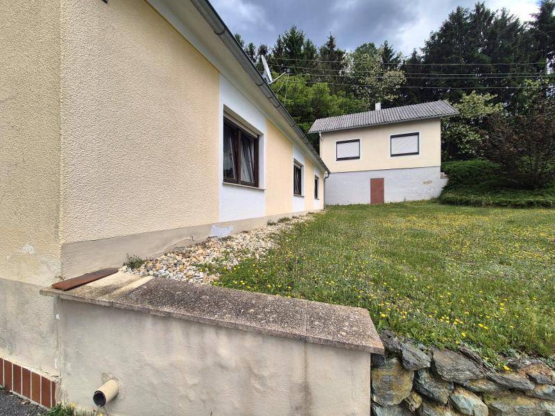 Seitenansicht des Hauses mit gelber Fassade, Kiesbeet und einem weiteren Gebäude im Hintergrund.