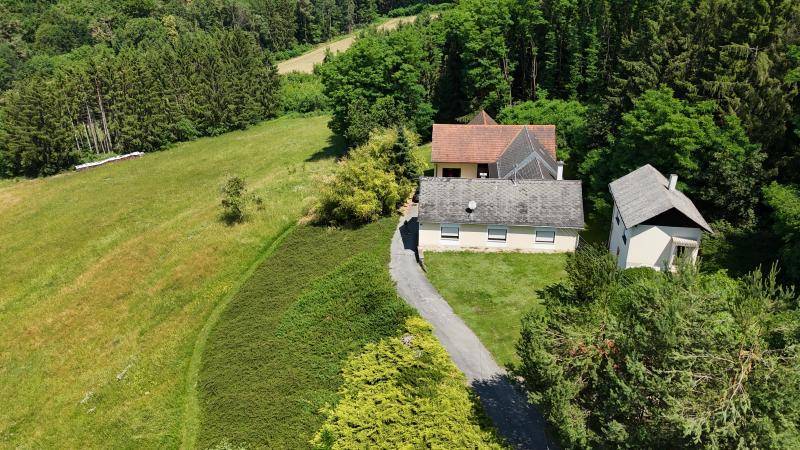 Luftaufnahme eines Anwesens mit mehreren Gebäuden, umgeben von grünen Feldern und dichtem Wald.