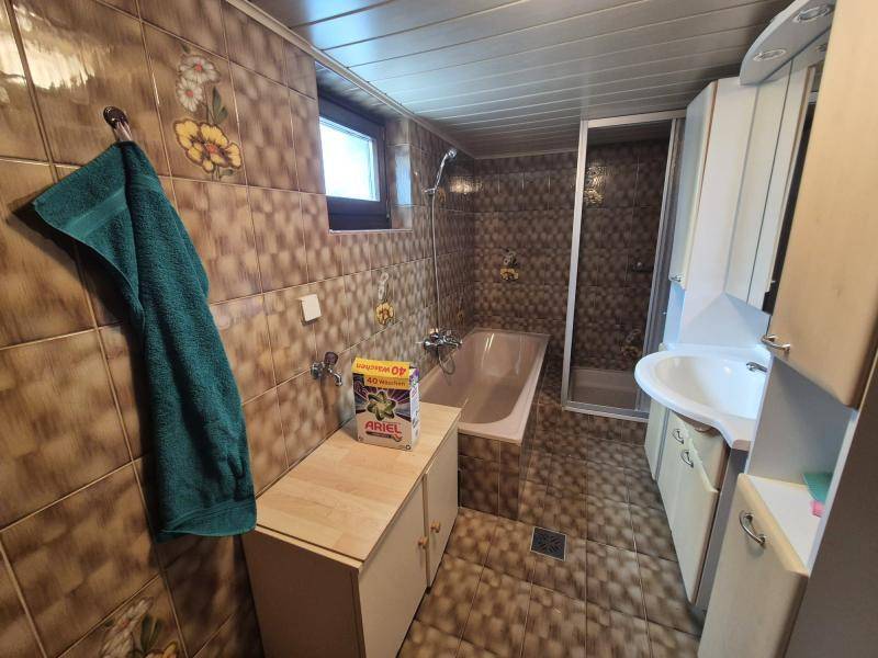 Badezimmer mit braunen Fliesen, Badewanne, Duschkabine und einem kleinen Fenster.