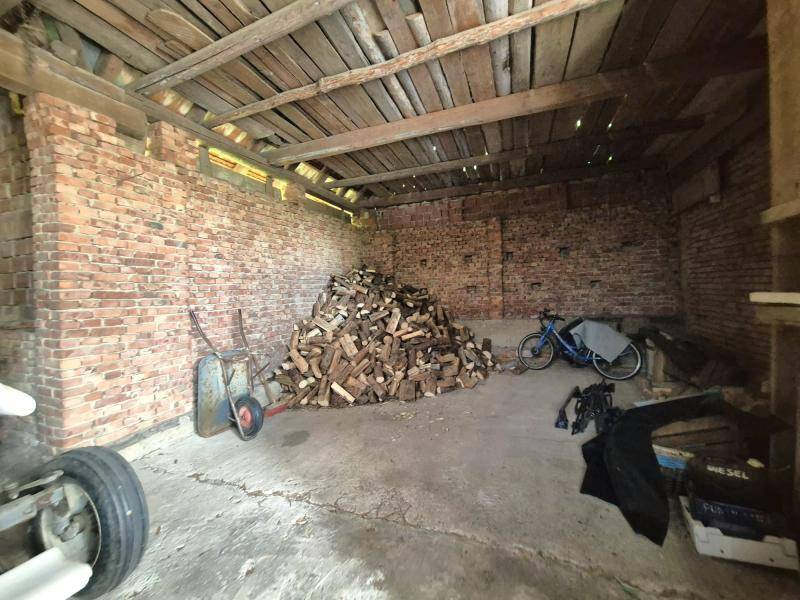 Großer Scheunenbereich mit Ziegelwänden, Holzbalken und einem Stapel Brennholz.