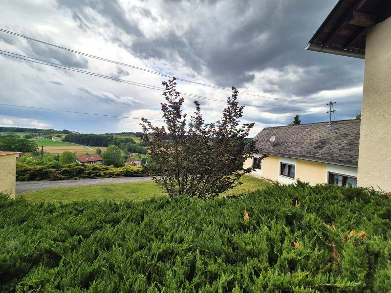 Blick vom Grundstück auf die umliegende Landschaft mit Feldern und einem Haus unter bewölktem Himmel.