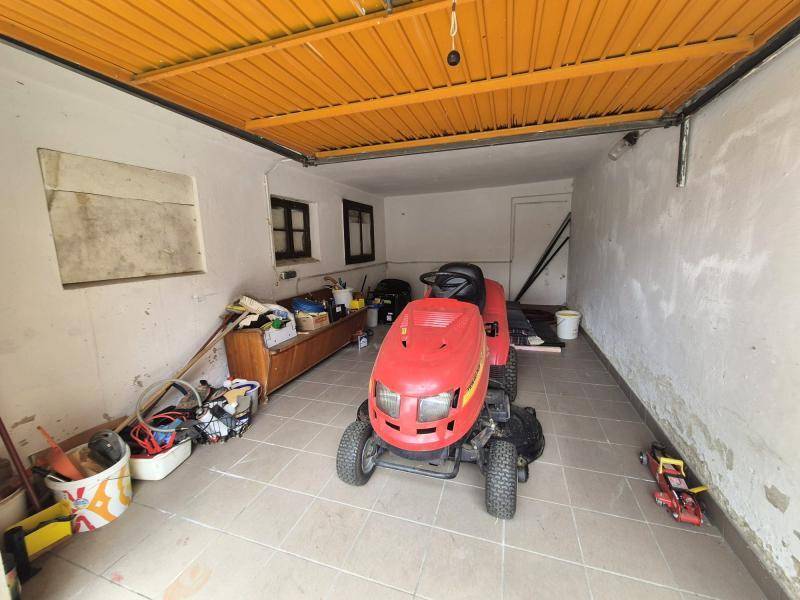 Geräumige Garage mit Fliesenboden, einem Rasenmäher und Stauraum an den Wänden.