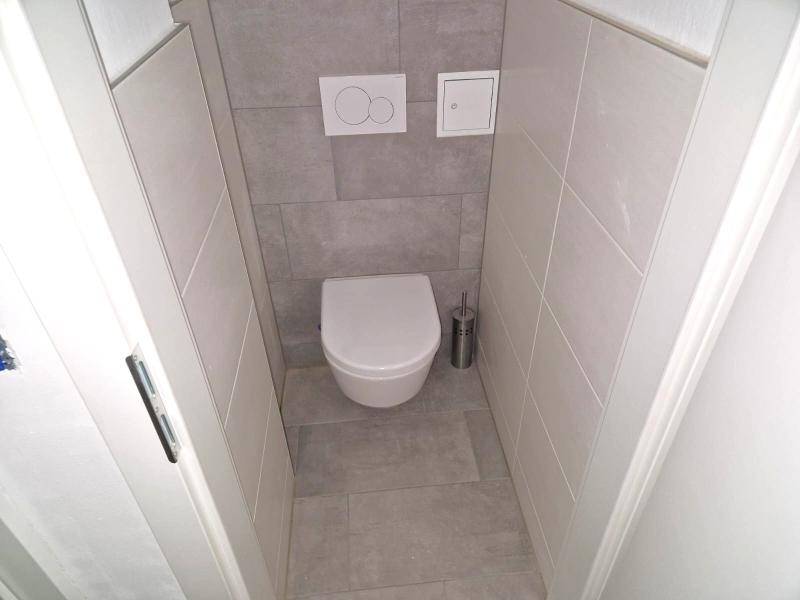 Separate Toilette mit Wand-WC und modernen grauen Fliesen, minimalistisch und funktional gestaltet.