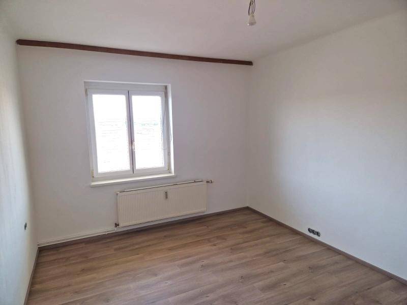 Unmöbliertes Zimmer mit Laminatboden, Fenster und Heizkörper, ideal als Schlaf- oder Arbeitszimmer.