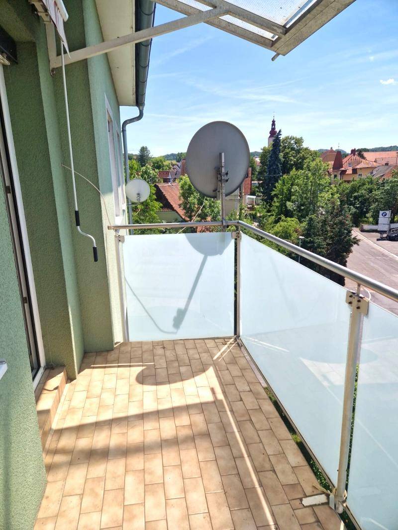 Kleiner Balkon mit Fliesenboden und Blick auf die Dächer der Nachbarschaft und einen Kirchturm.