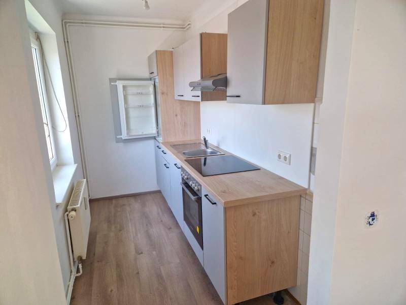 Funktionale Küche mit hellen Holz- und Grautönen, integriertem Kochfeld und Backofen.