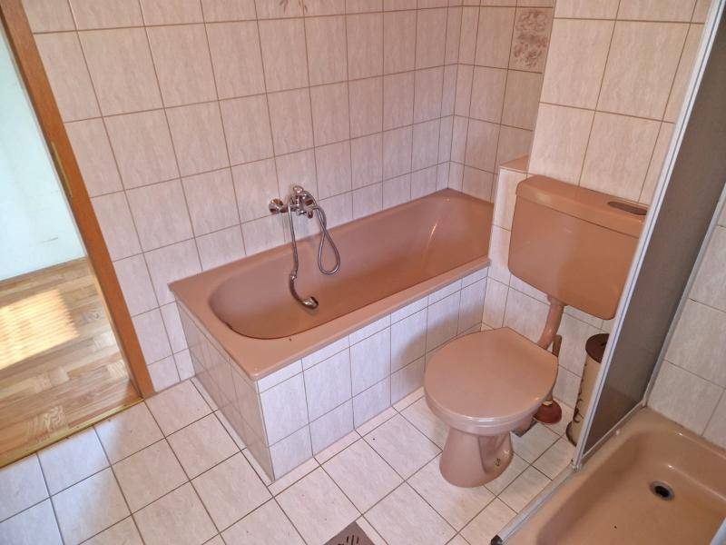 Badezimmer mit beigefarbenen Fliesen, Badewanne und Toilette im 80er-Jahre-Stil.
