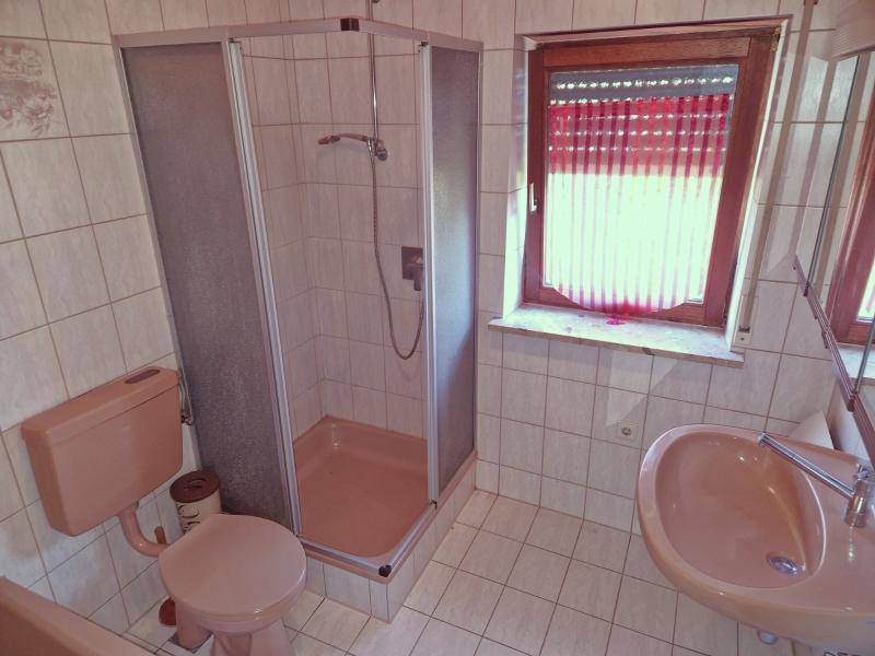 Badezimmer mit beigefarbenen Fliesen, Duschkabine, Toilette und Fenster.