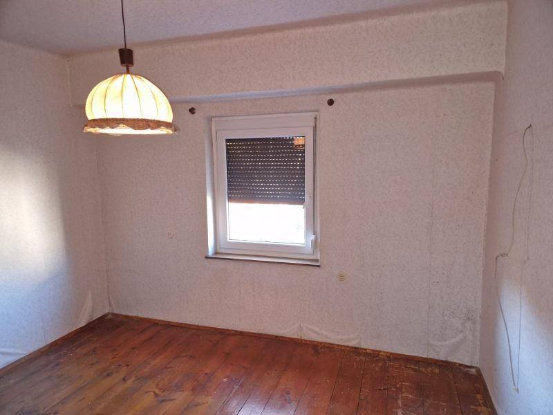 Leerer Raum mit Holzboden, Fenster mit Rollladen und einfacher Deckenleuchte.
