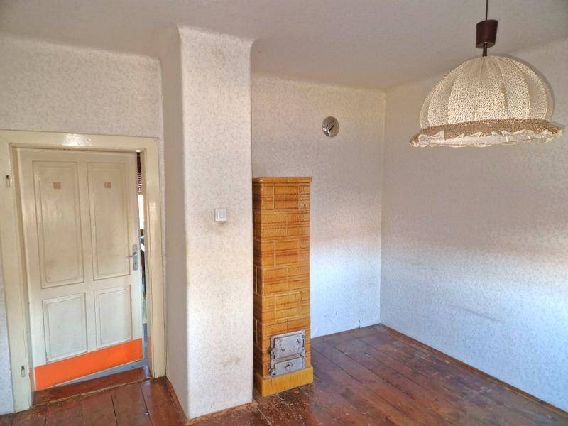 Leerer Raum mit Holzboden und einem traditionellen Kachelofen, bereit für Renovierung.
