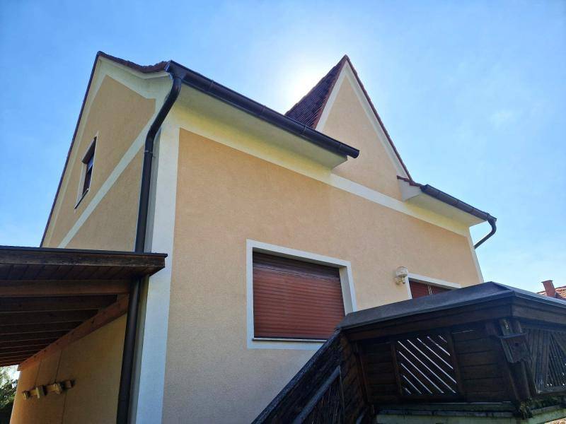 Detailansicht der Hausfassade mit Dachüberstand und Rollladen an einem sonnigen Tag.