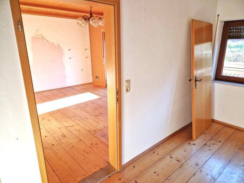 Heller Raum mit Holzboden und Holztäfelung an der Decke, bereit für Renovierung.