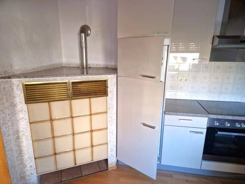 Küchenzeile mit Kühlschrank, Spüle und einem traditionellen Kachelofen im Eckbereich.