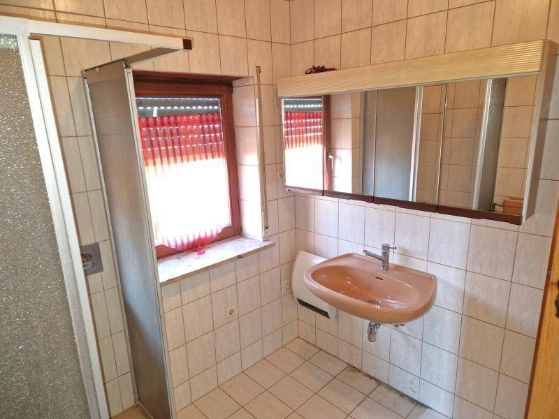 Badezimmer mit beigefarbenen Fliesen, Waschbecken, Spiegel und Fenster.
