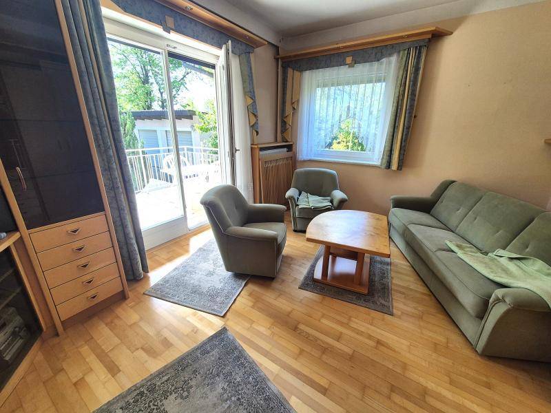 Helles Wohnzimmer mit bequemen Sitzmöbeln, Parkettboden und Blick ins Grüne durch das Fenster.