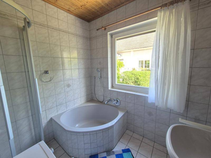 Helles Badezimmer mit Eckbadewanne, Duschkabine und Fenster, das Tageslicht hereinlässt.