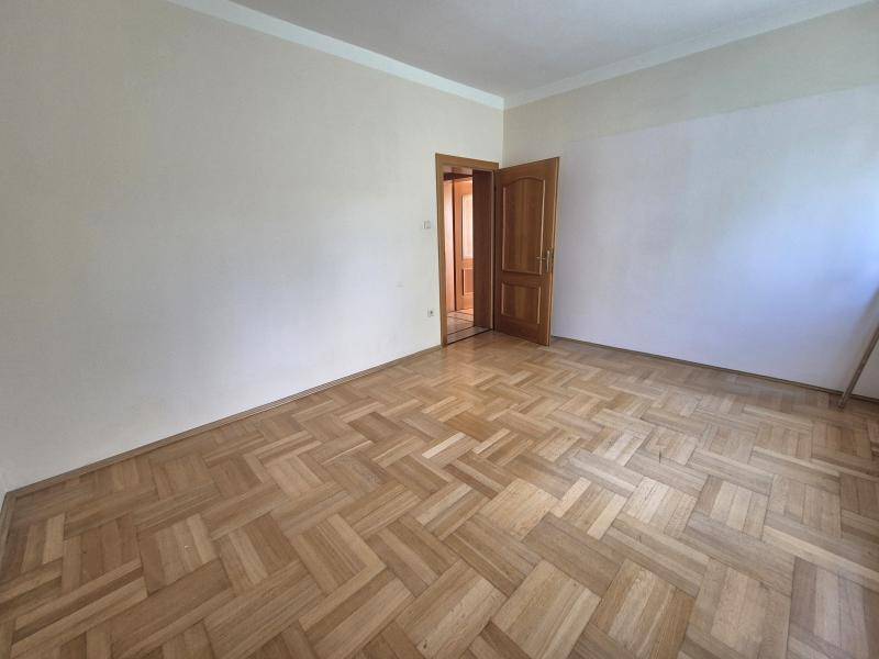 Leeres Zimmer mit klassischem Fischgrätparkett und einer Holztür, bereit zur individuellen Gestaltung.