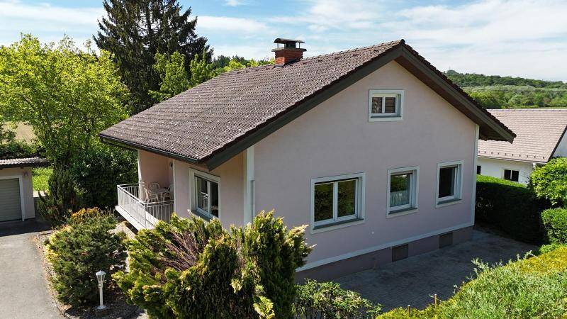 Seitenansicht des Hauses mit Balkon, umgeben von üppigem Grün und Bäumen.