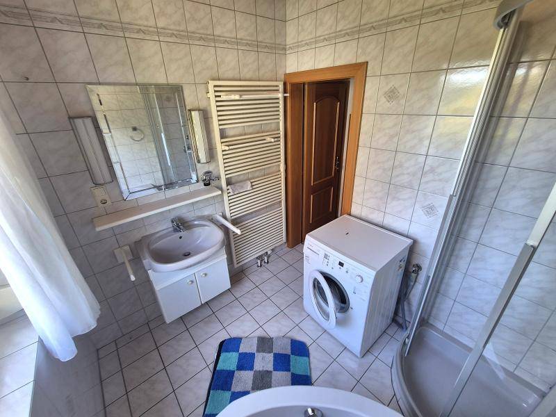 Badezimmer mit Waschbecken, Spiegel, Handtuchheizkörper, Waschmaschine und Duschkabine.