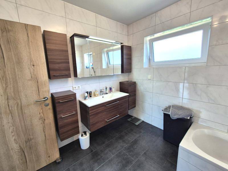Helles Badezimmer mit modernem Waschtisch, Spiegelschrank und Fenster.