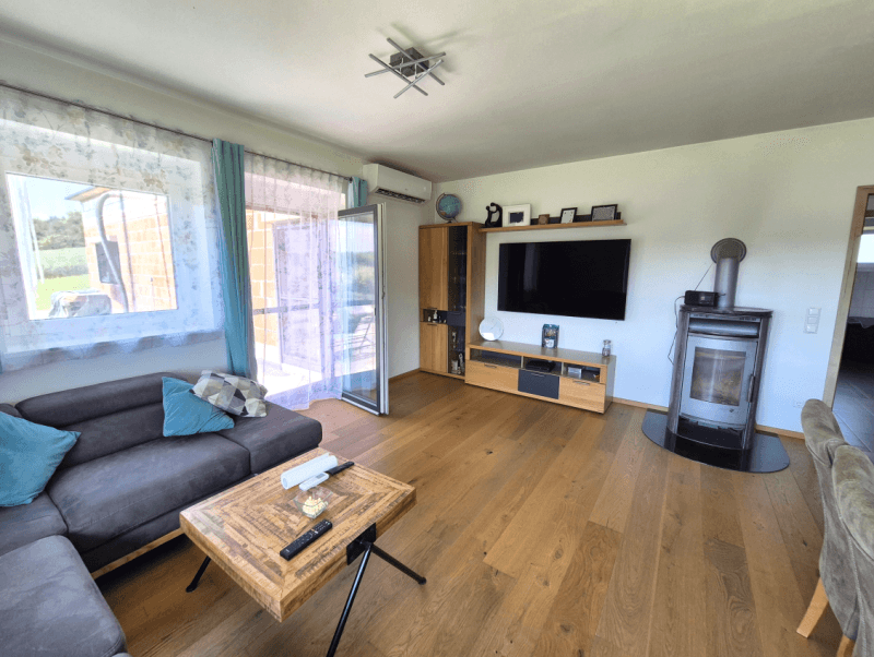 Gemütliches Wohnzimmer mit Holzboden, Kaminofen und Zugang zum Außenbereich.