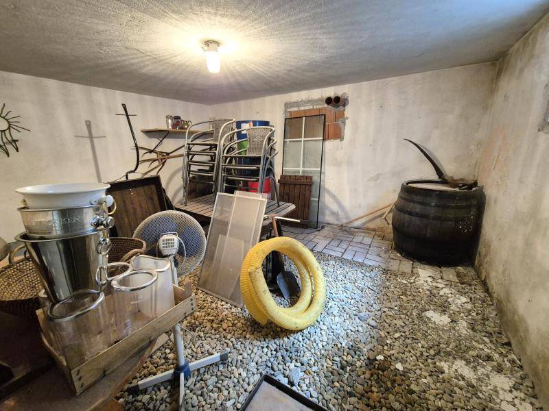 Rustikaler Kellerraum mit Kies- und Fliesenboden, verschiedenen Gegenständen und einem Holzfass.