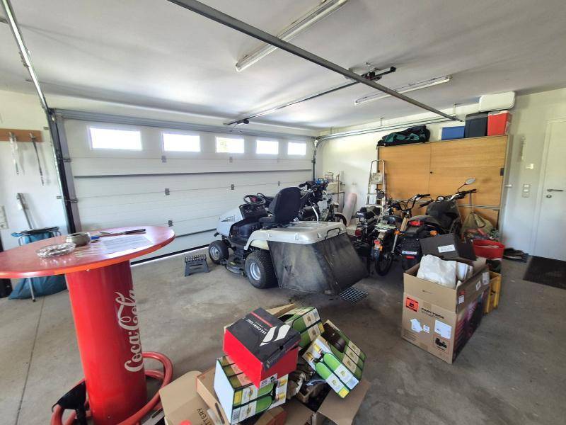 Geräumige Garage mit Rasenmäher, Motorrädern und verschiedenen Lagerboxen, ideal für Hobby und Lagerung.