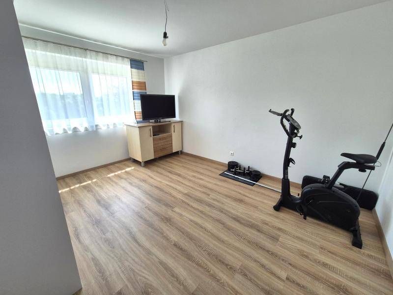Geräumiges Zimmer mit Holzboden, Fenster und Fitnessgerät.