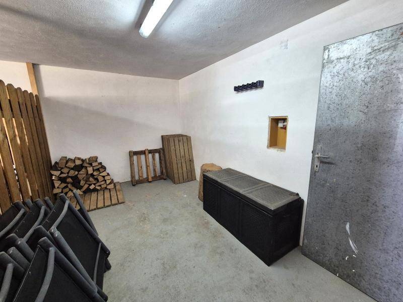 Kellerraum mit Holzstapeln, Klappstühlen und einer robusten Metalltür, ideal für Lagerzwecke.
