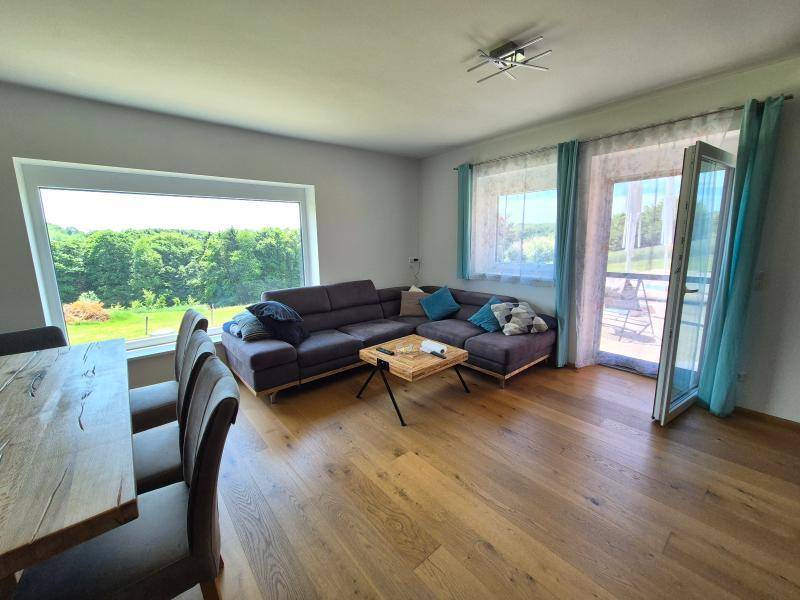 Helles Wohn- und Esszimmer mit Holzboden, großem Fenster und Zugang zur Terrasse.
