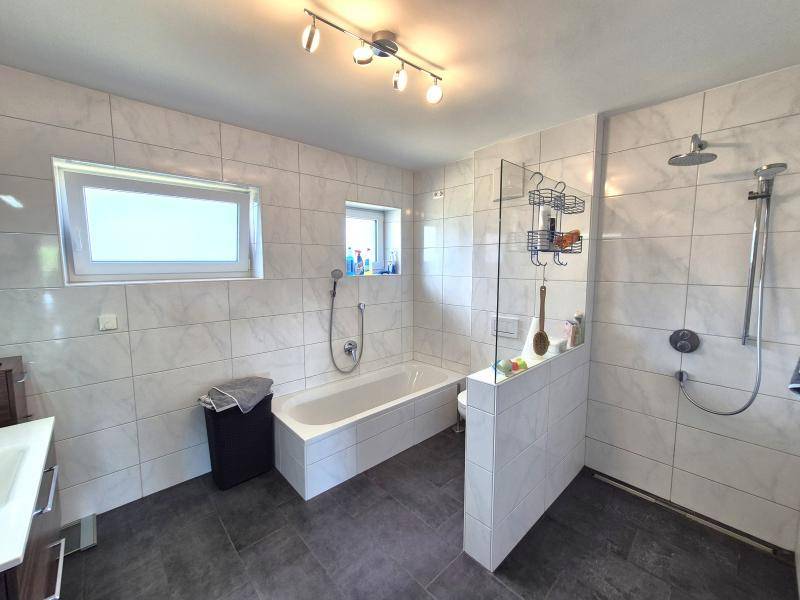 Modernes Badezimmer mit Badewanne, Dusche und hellen Fliesen.