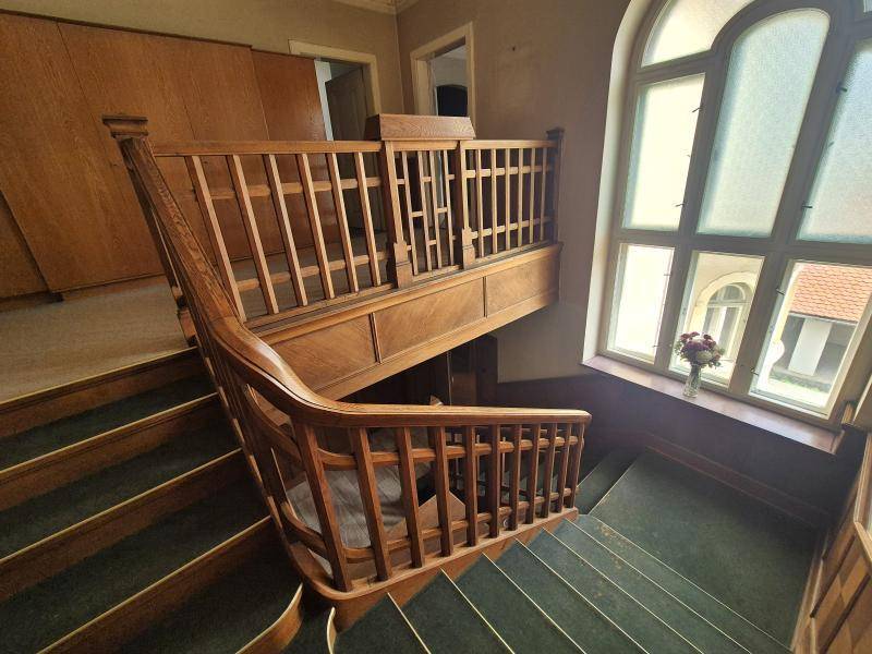 Historisches Treppenhaus mit Holzgeländer, Teppichstufen und großem Bogenfenster.