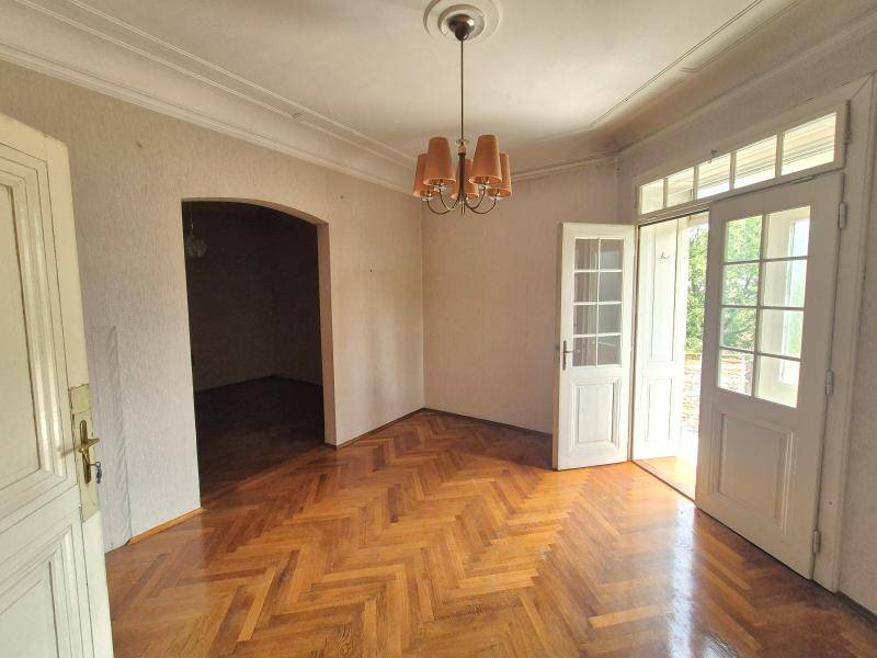 Geräumiges Wohnzimmer mit Fischgrätparkett, hohen Decken und Zugang zu einem Balkon.