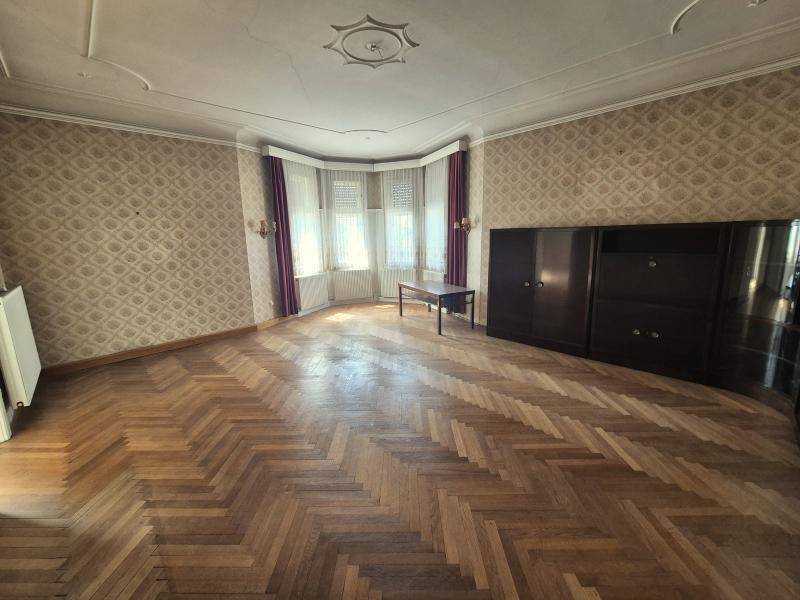 Großes Wohnzimmer mit Fischgrätparkett, Erkerfenstern und gemusterter Tapete.