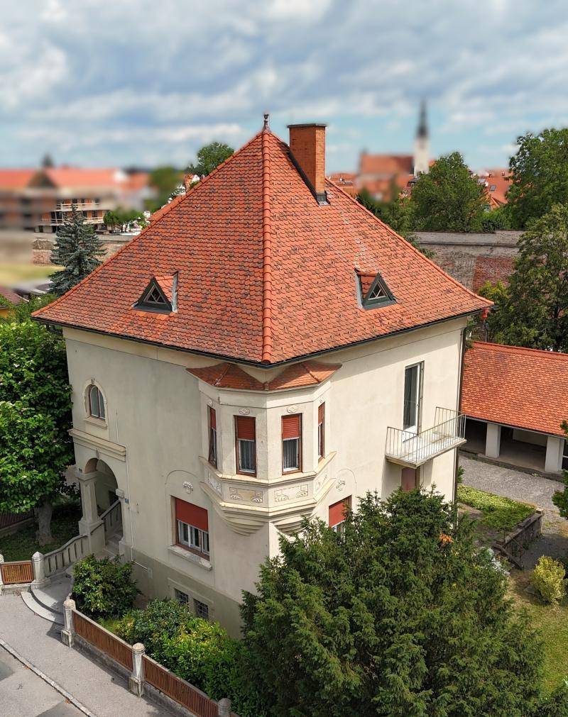 Elegante Villa mit rotem Ziegeldach und dekorativen Fenstern in einer ruhigen Wohngegend.