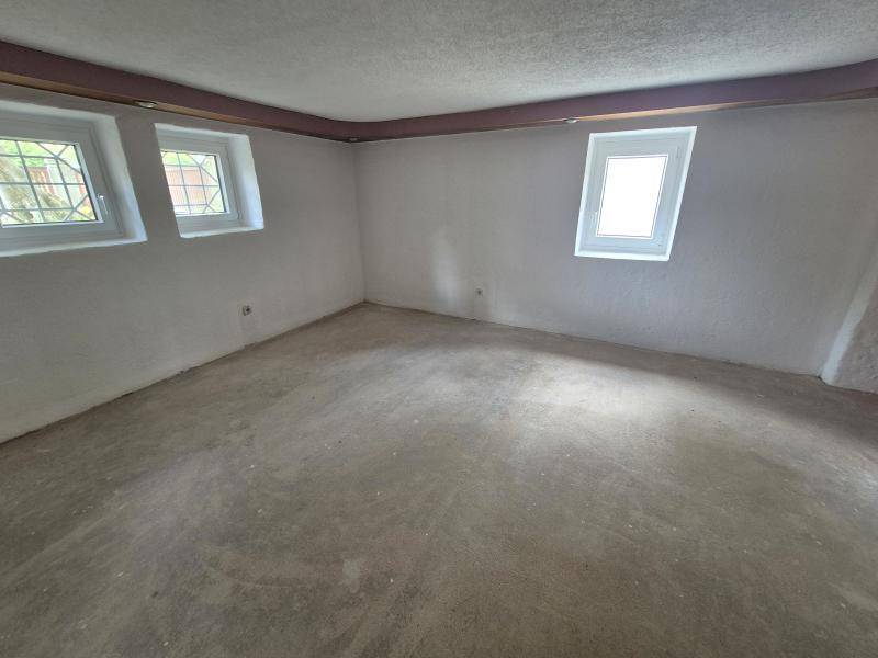 Leerer Kellerraum mit Betonboden und kleinen Fenstern, bereit für den Ausbau.