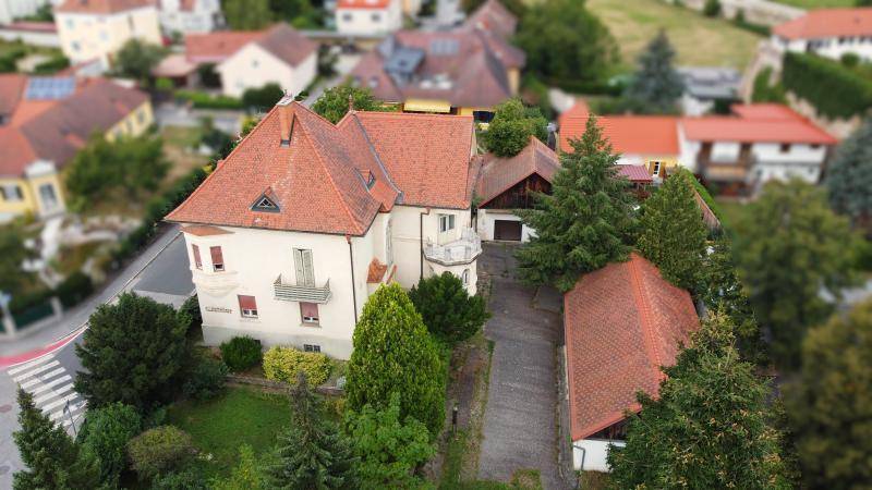Große Villa mit Nebengebäuden und weitläufigem Grundstück, umgeben von viel Grün.